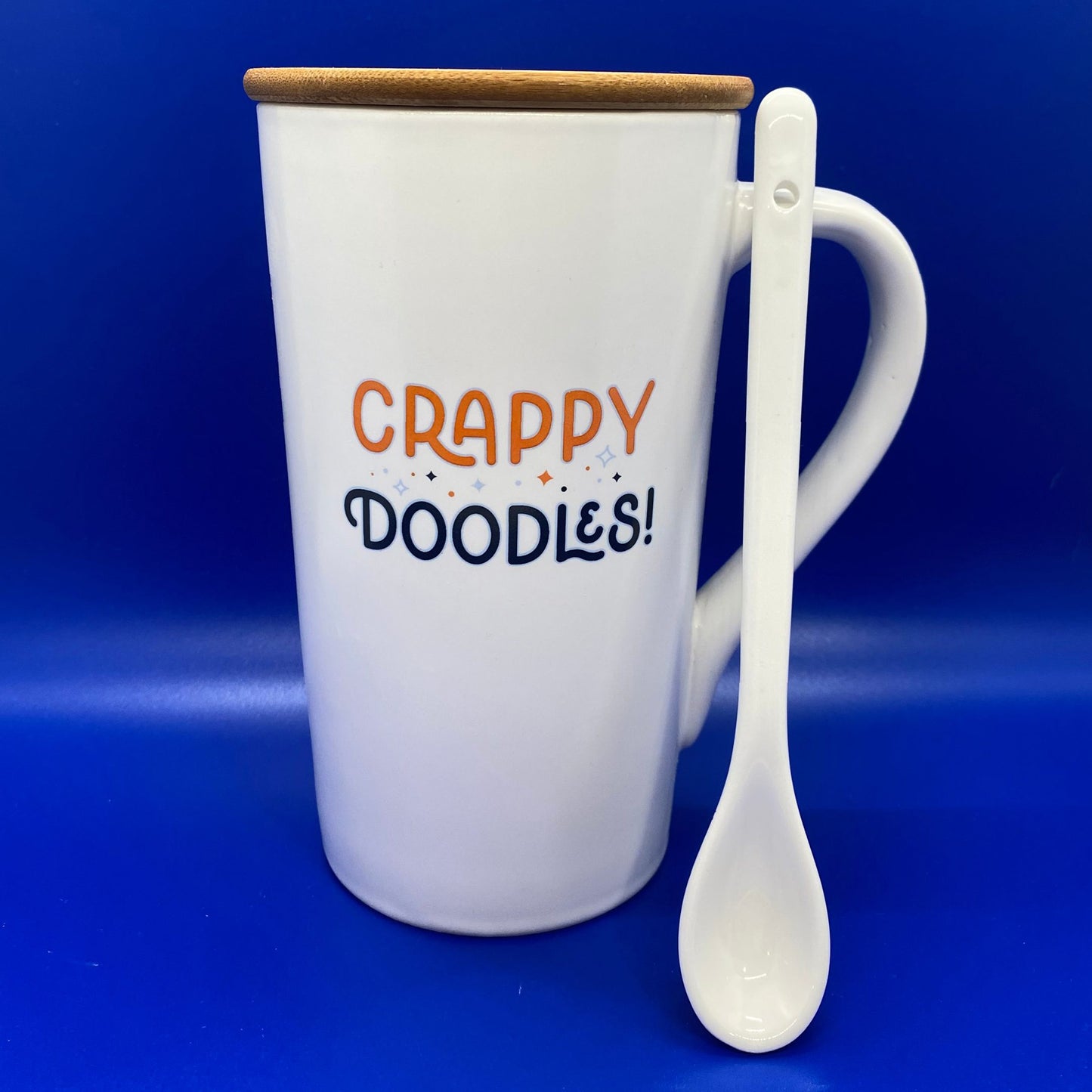 White mug with 'CRAPPY DOODLES!' text and wooden lid on a blue background