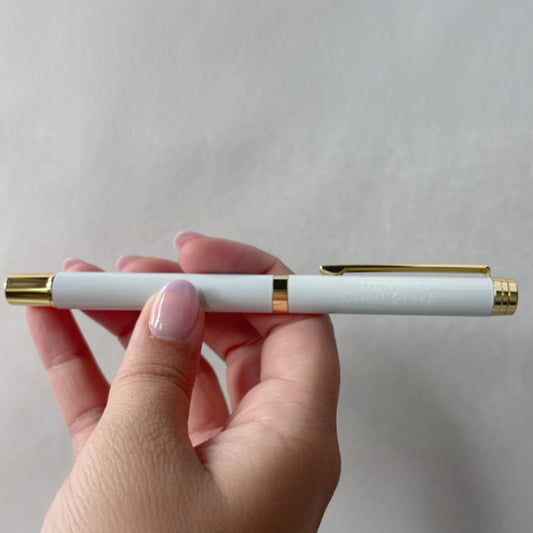 Hand holding a white pen with gold accents against a light gray background