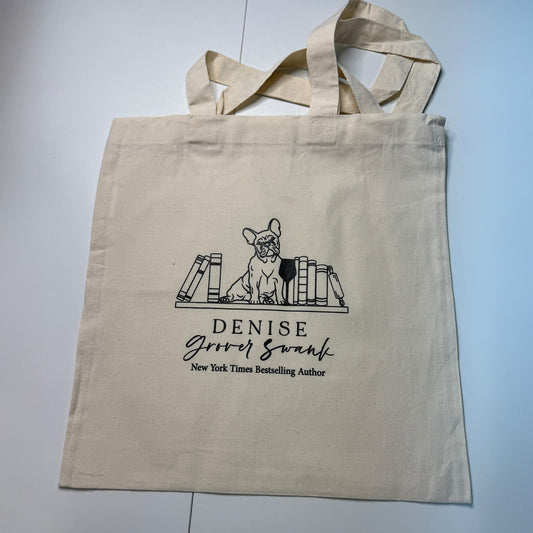 Beige tote bag with a design of a dog sitting on books and text on a light gray background